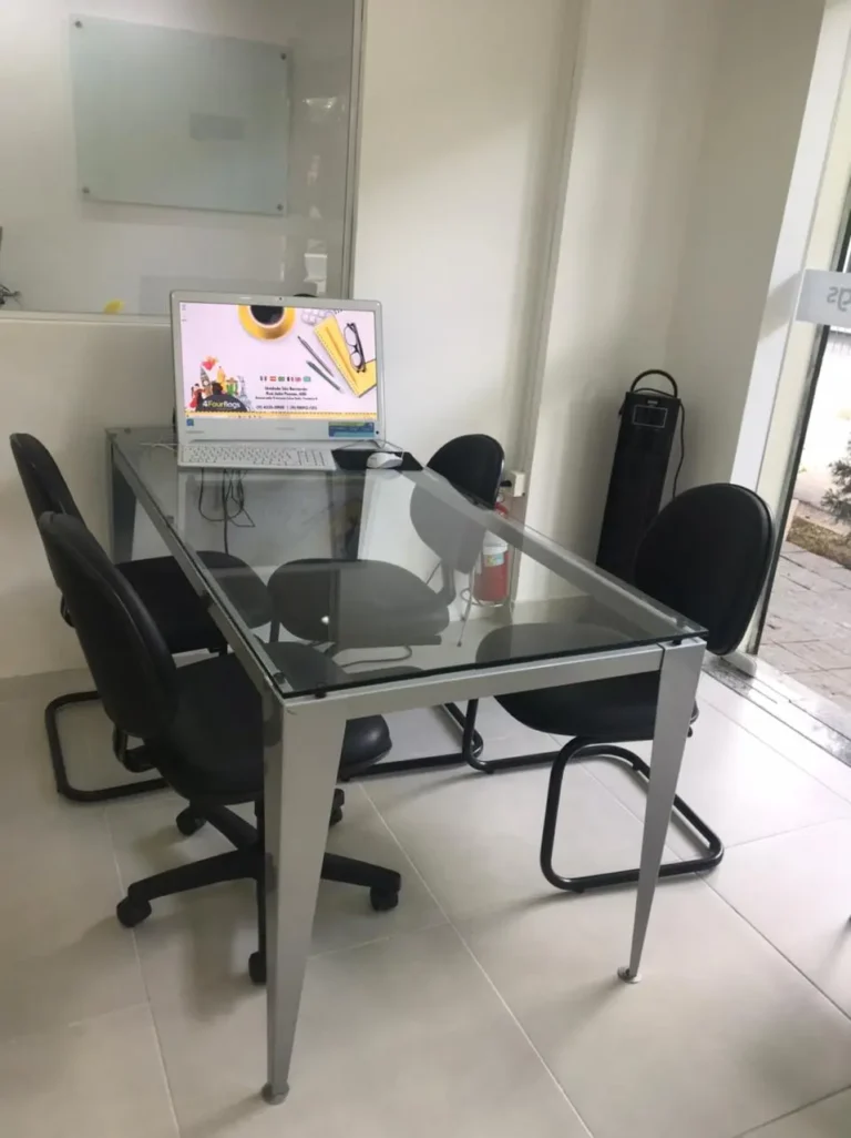 Sala de aula estilo executivo na FourFlags São Bernardo do Campo, com mesa de reunião em vidro e computador para aulas dinâmicas de idiomas.
